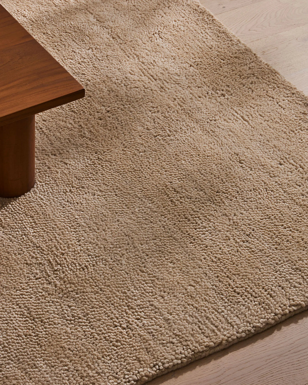 Neutral wool rug with woven texture anchors a minimalist living space, pairing warm taupe tones with rich timber furniture and light timber flooring