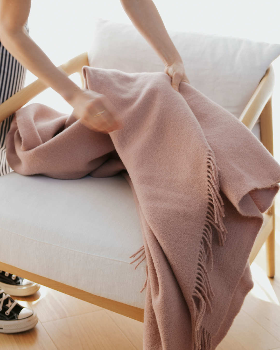 Nevis Rose throw in soft blush pink with tassel border detail, draped across white bed by Weave Home