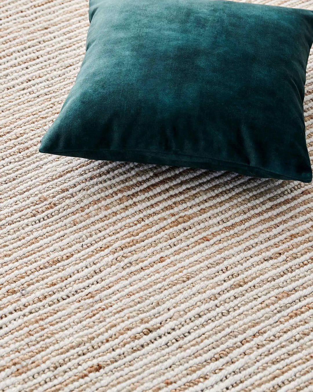 Emerald velvet cushion on natural textured jute rug, layered neutral and teal colour palette with woven fabric texture detail