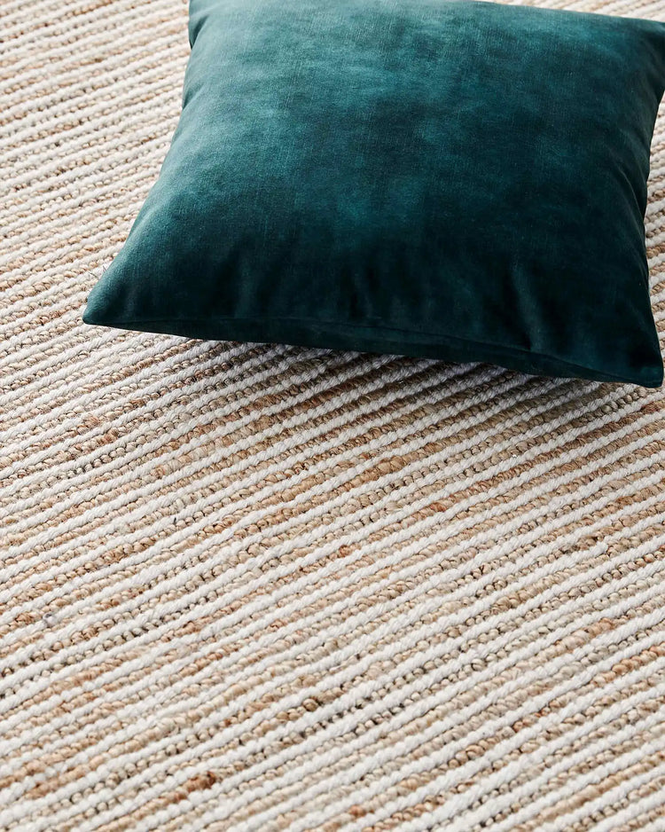 Emerald velvet cushion on natural textured jute rug, layered neutral and teal colour palette with woven fabric texture detail