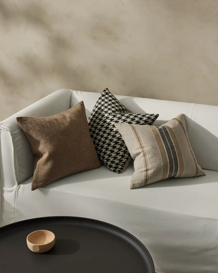 Neutral modern bedroom with white curved sofa styled with three cushions: earthy textured Domenica, monochrome houndstooth Giovanni, and striped Franco in warm naturals and greys
