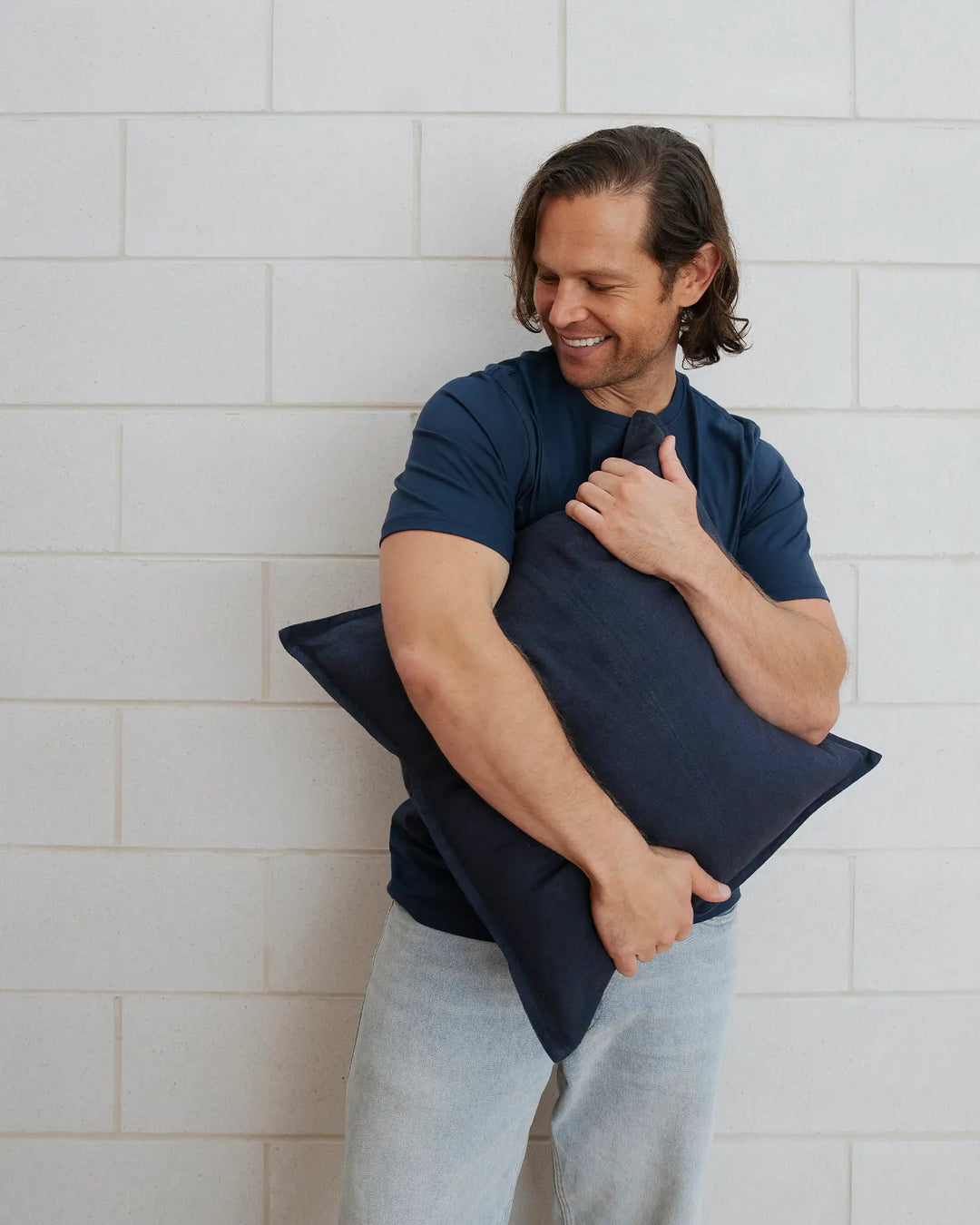 Como Ocean cushion in navy blue European linen, held by man against white brick wall, by Weave Home