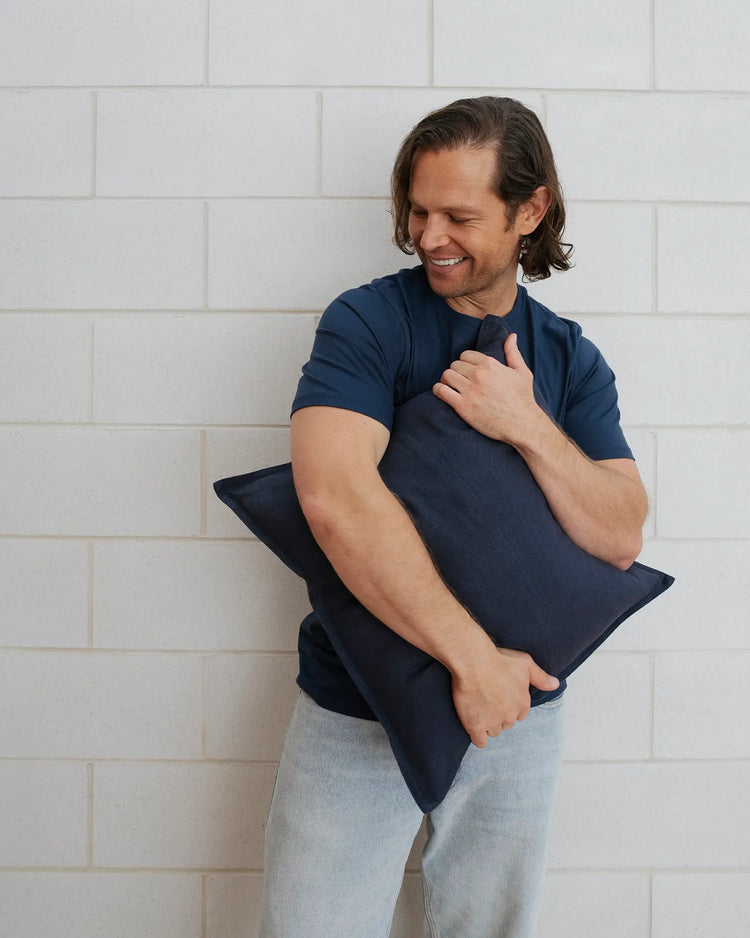 Como Ocean cushion in navy blue European linen, held by man against white brick wall, by Weave Home