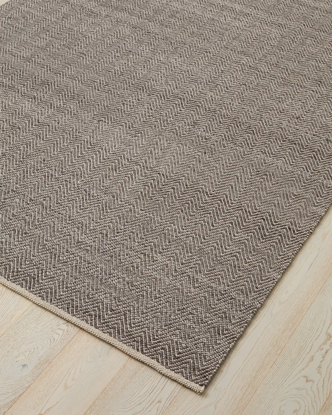 Matterhorn Tar chevron rug corner detail, showing two-toned grey wool-cotton weave with cotton braided edge by Weave Home