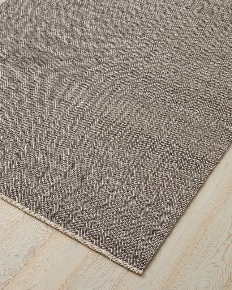 Matterhorn Tar chevron rug corner detail, showing two-toned grey wool-cotton weave with cotton braided edge by Weave Home