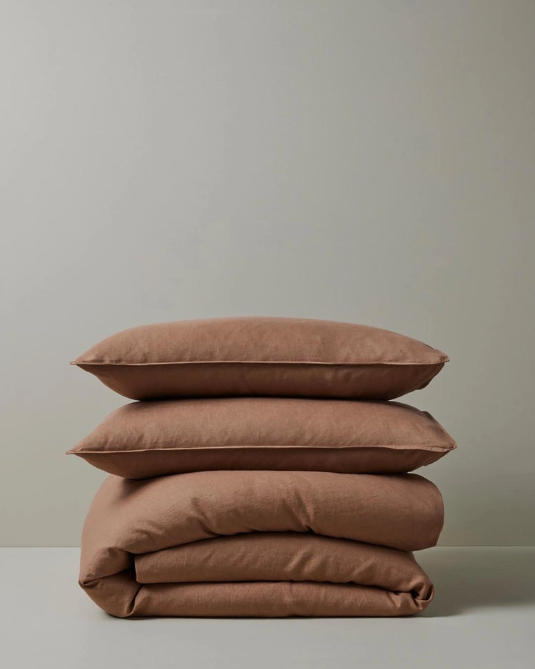 Stacked Ravello Quilt Cover and Pillowcase Set in biscuit, showcasing warm terracotta and neutral tones with soft linen texture and minimalist styling