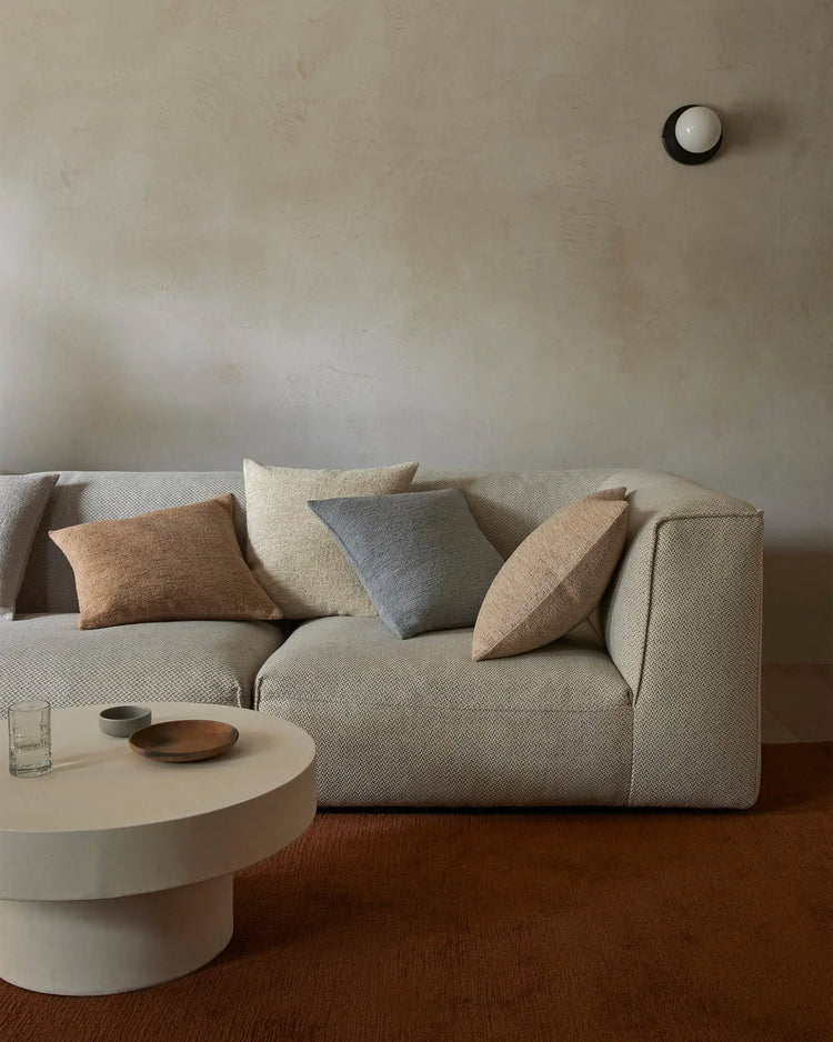 Neutral living room styled with cream sofa, warm terracotta and grey cushions, and earthy wool rug; minimalist aesthetic with textured fabrics