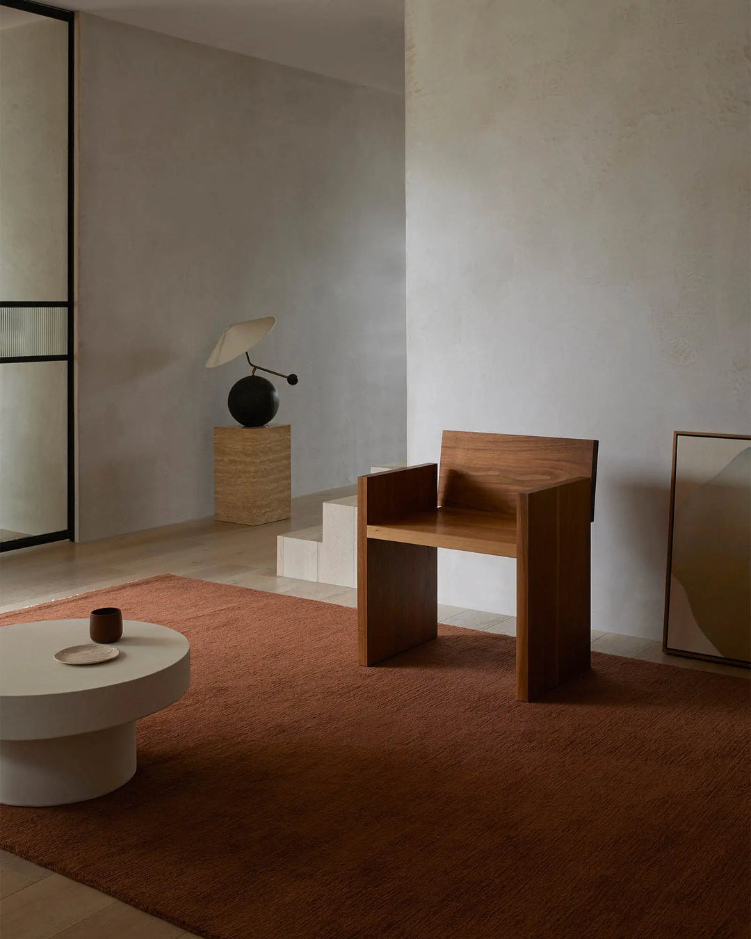 Terracotta wool rug grounds a minimalist interior with warm earthy tones, natural wood furniture, and soft neutral textiles creating a serene, gallery-like living space