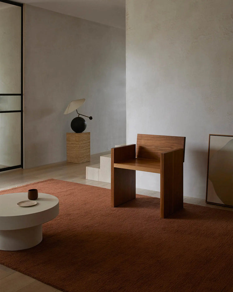 Terracotta wool rug grounds a minimalist interior with warm earthy tones, natural wood furniture, and soft neutral textiles creating a serene, gallery-like living space
