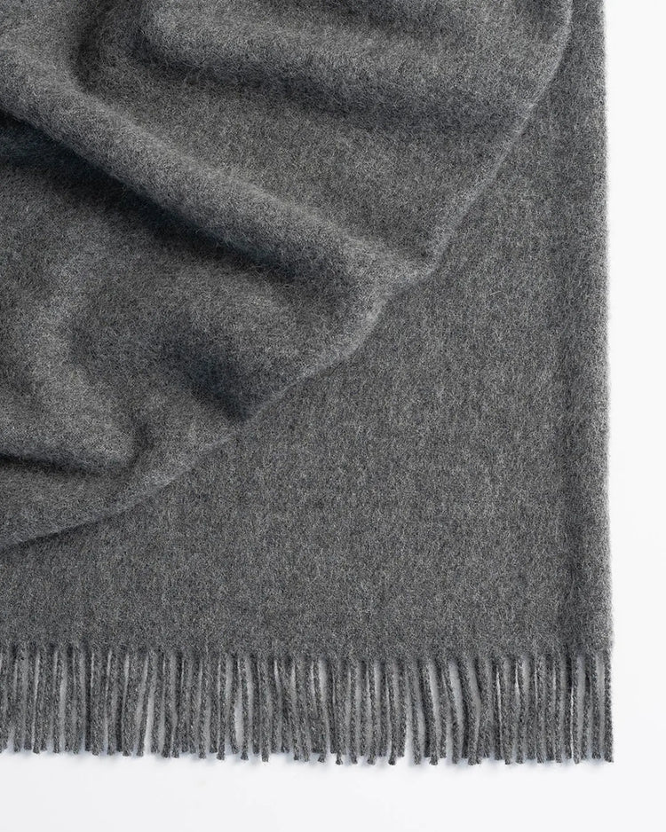 Nevis Charcoal throw in mid-toned grey lambswool with tassel fringe border, textured weave detail by Weave Home