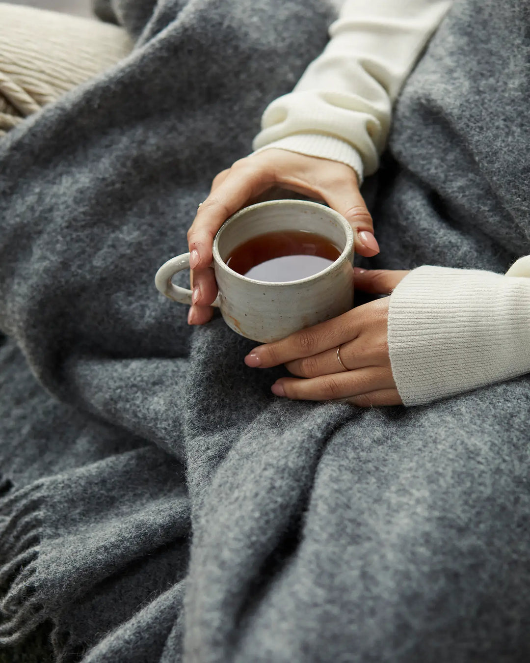 Charcoal wool throw layered over cream knitwear, styled with ceramic mug of tea for a cosy monochrome aesthetic with warm neutral accents