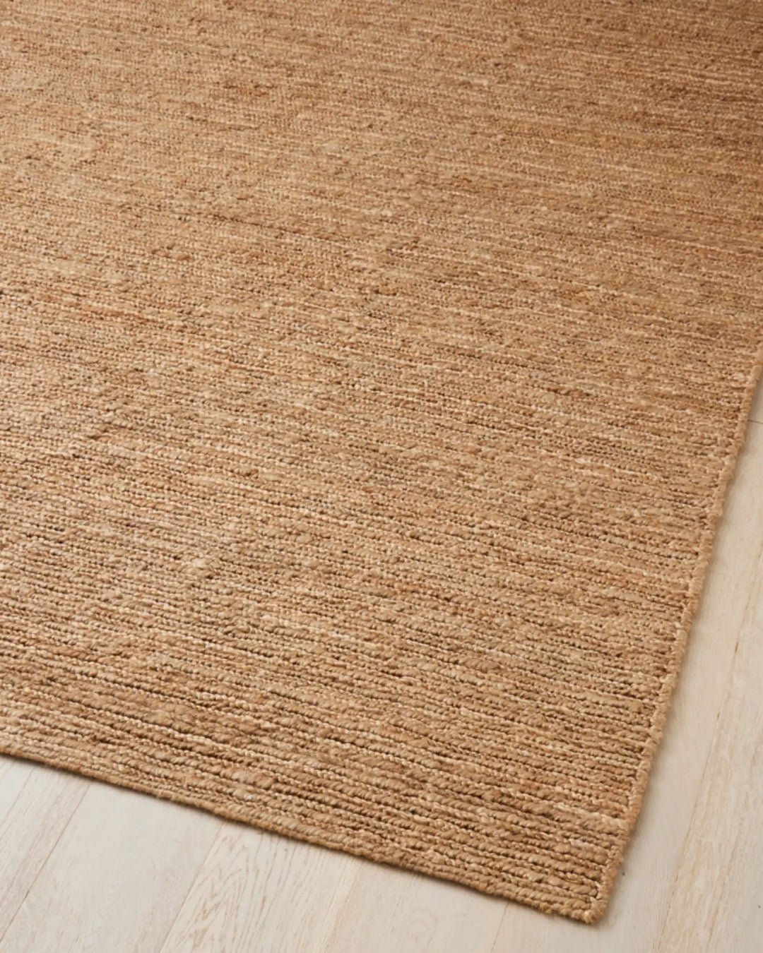 Suffolk Natural jute rug in golden brown, corner detail showing textured weave and cotton edging on light floor by Weave Home