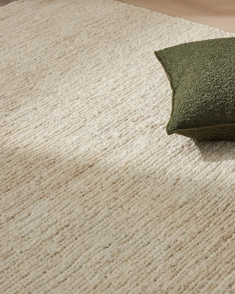 Cream jute rug with textured weave and olive green cushion, showcasing natural neutral palette and organic materials for minimalist home styling