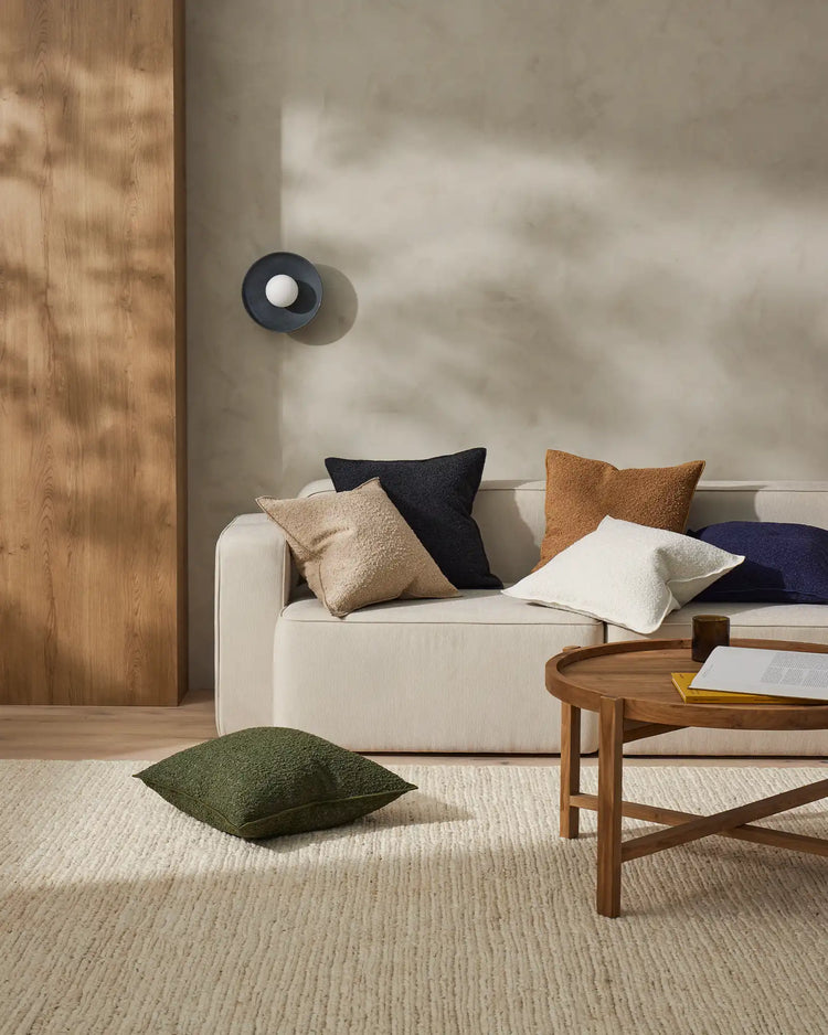 Scandinavian living room with cream sofa styled with olive, charcoal, caramel and ivory Alberto cushions, neutral jute rug, timber coffee table and wooden wall panelling