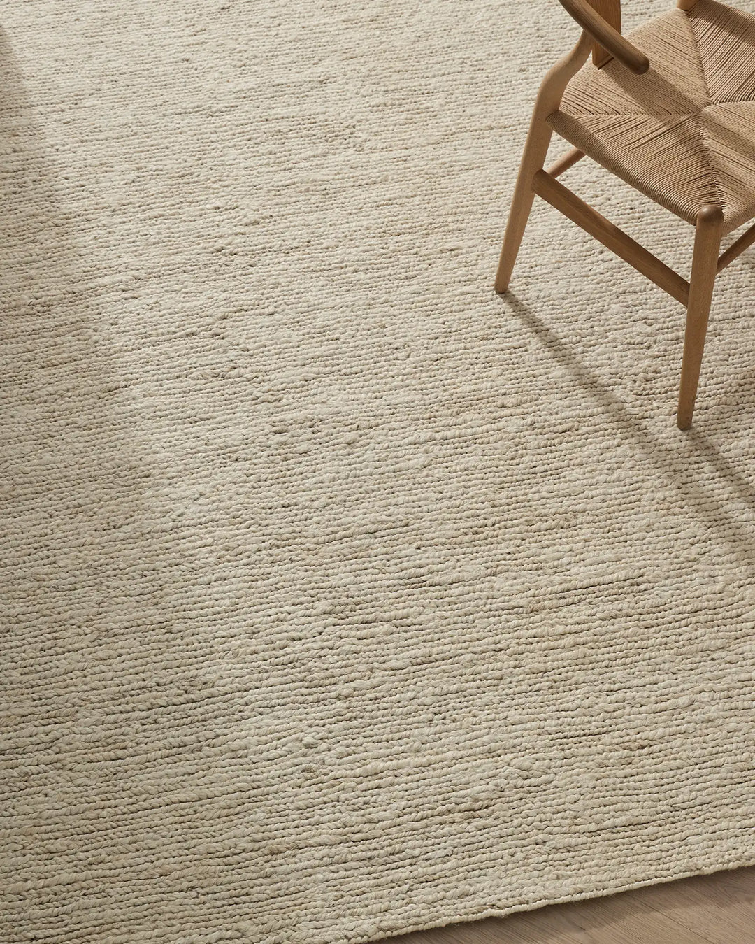 Minimalist Scandinavian interior with natural jute texture rug in cream, woven chair with rush seat, and warm timber legs casting soft shadows on neutral flooring.