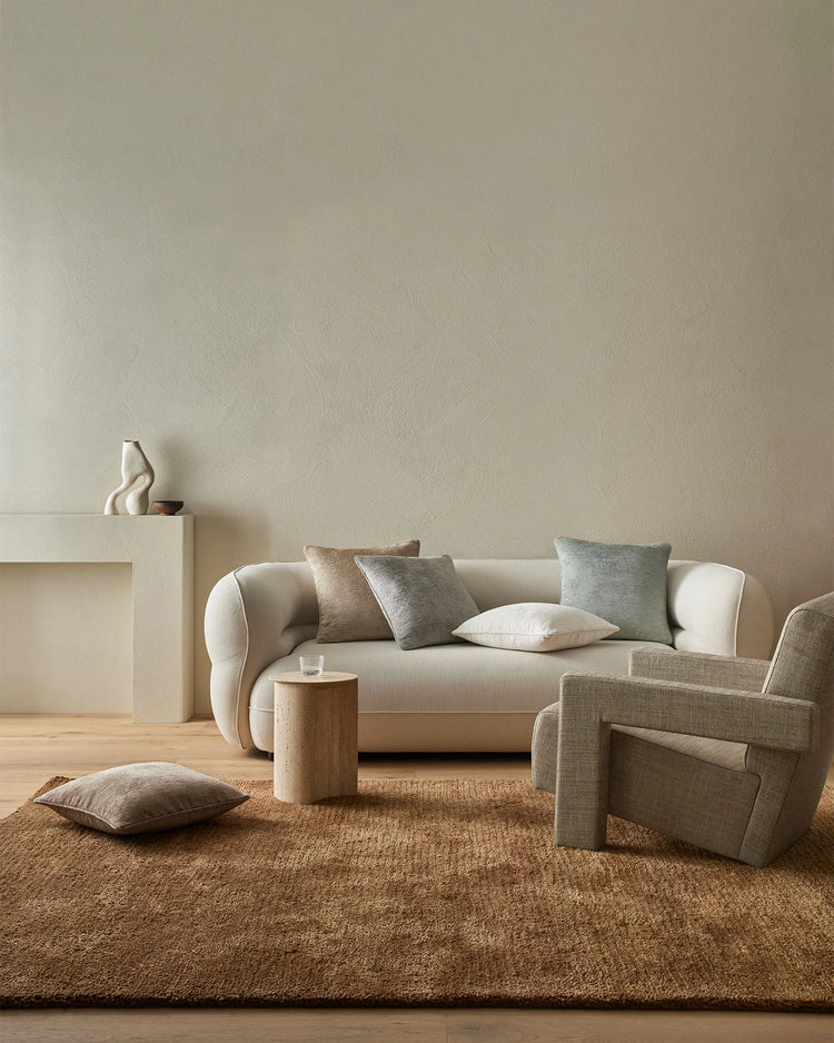 Neutral living room with cream curved sofa and taupe armchair layered with Tempo cushions in mink and gull tones, jute rug, and natural wood accents for calm minimalist interiors