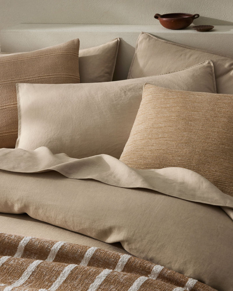 Neutral bedding styling with layered linen pillows and Ravello Quilt Cover in cream and natural tones, striped throw detail, warm minimalist bedroom aesthetic