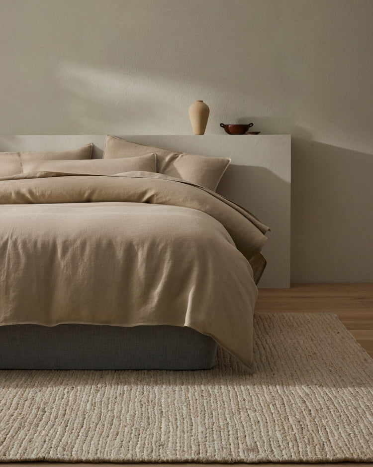 Minimalist bedroom with neutral linen bedding, textured jute rug, and earthy pottery styling, warm beige palette and calm aesthetic