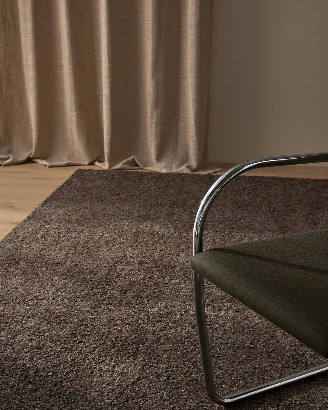 Neutral minimalist living room with chocolate wool blend Marceau rug, taupe linen curtains, and natural wood floor creating warm earth-tone palette