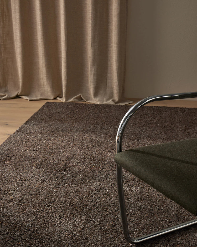 Neutral minimalist living room with chocolate wool blend Marceau rug, taupe linen curtains, and natural wood floor creating warm earth-tone palette