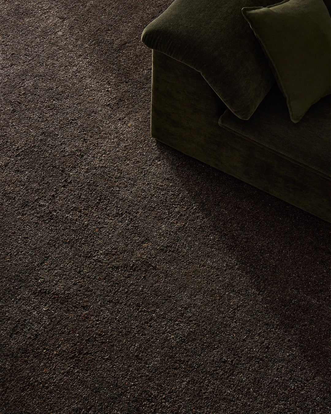 Charcoal wool blend rug with deep chocolate tones anchoring a moody living space, styled with olive velvet cushions for layered texture and earthy sophistication