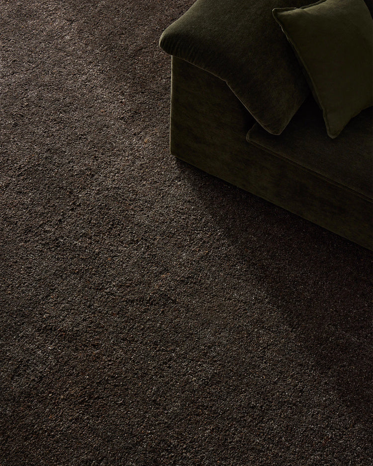 Charcoal wool blend rug with deep chocolate tones anchoring a moody living space, styled with olive velvet cushions for layered texture and earthy sophistication