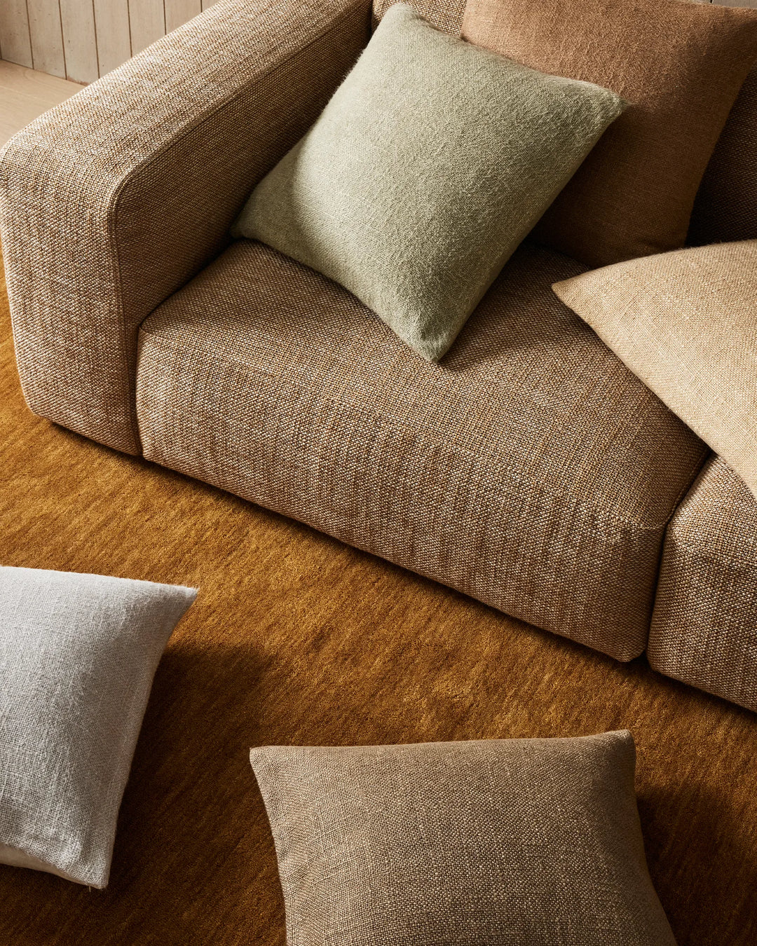 Neutral living room scene with warm terracotta rug, taupe linen sofa, and Domenica cushions in sage, clay, glacier and natural—layered earthy tones and tactile weaves