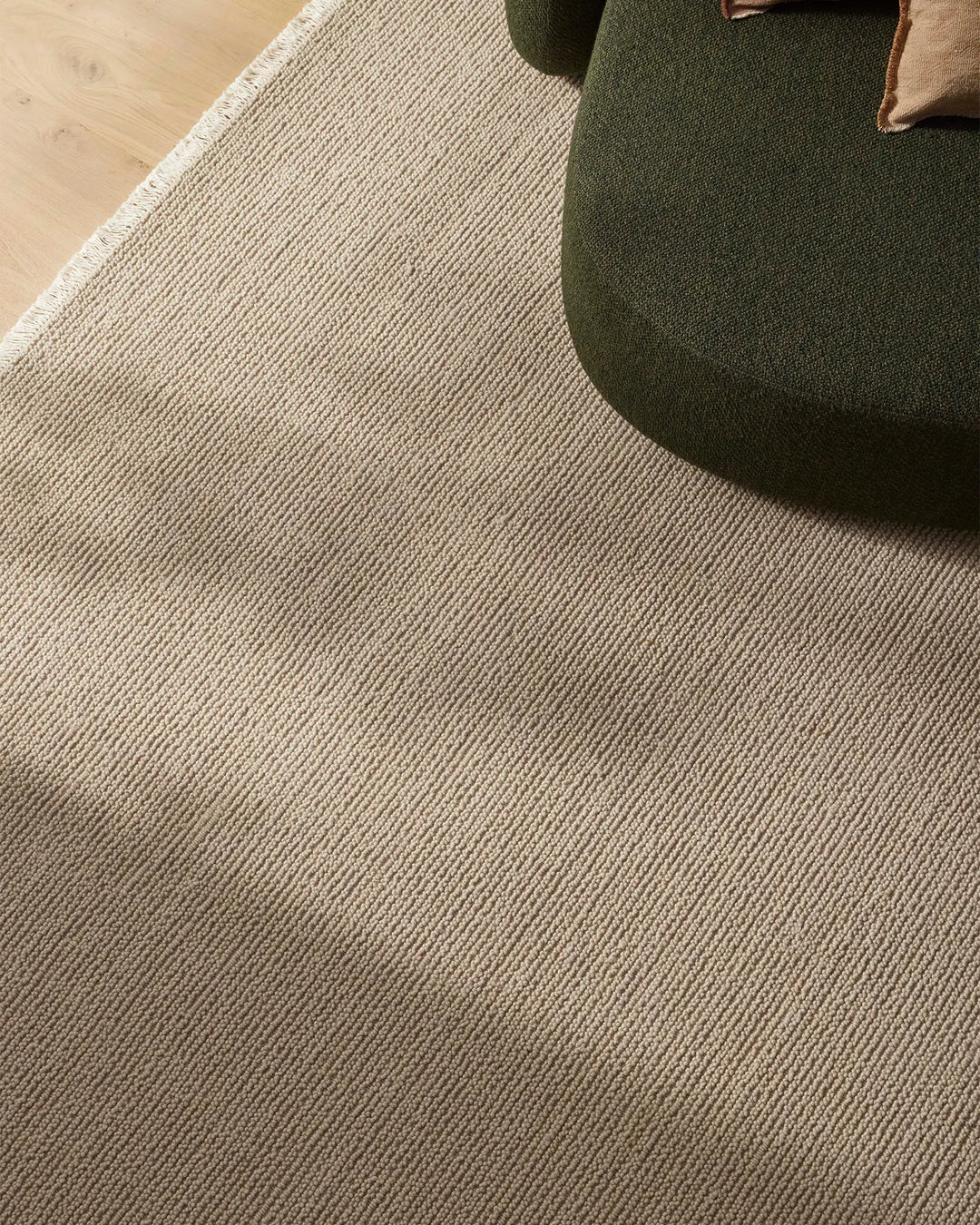 Neutral wool rug with fine linear texture anchoring a living space, styled with olive green upholstered seating and warm wood flooring for a contemporary, earthy aesthetic.