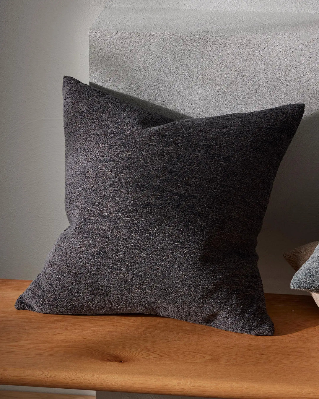 Charcoal cushion with soft textured weave styled on wooden shelf against white wall, showcasing neutral minimalist interior aesthetic