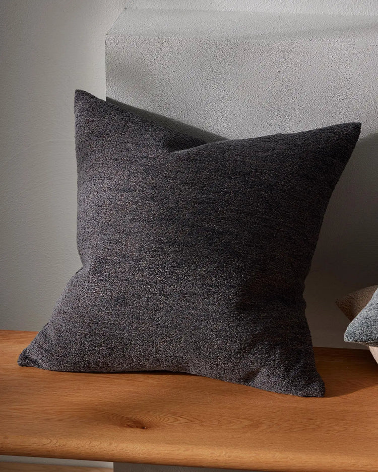 Charcoal cushion with soft textured weave styled on wooden shelf against white wall, showcasing neutral minimalist interior aesthetic