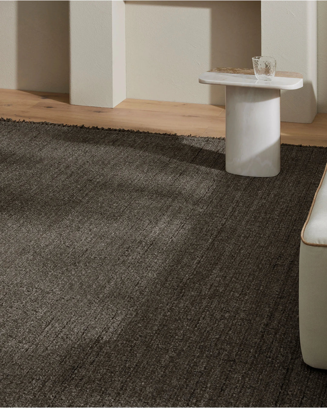 Minimalist room with charcoal textured wool-blend rug anchoring warm timber flooring, paired with cream architectural elements and white side table for serene Scandinavian-inspired interiors