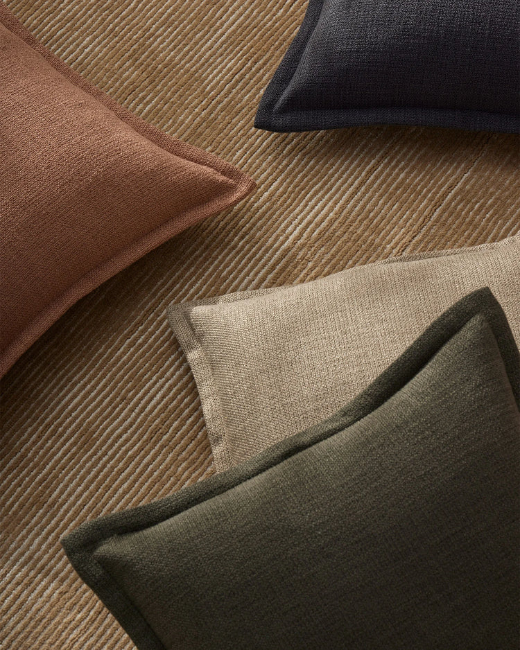 Figlio cushions in earthy and neutral tones arranged on textured rib-knit fabric, showcasing terra, midnight, oyster and kale polyester cushions in a warm, minimalist colour palette