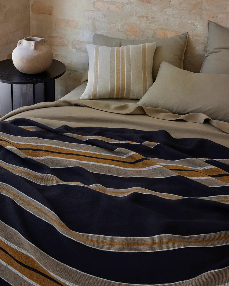 Neutral bedroom with textured brick wall, layered beige bedding and striped cushion, Franco throw in navy, ochre and cream stripe drape across bed