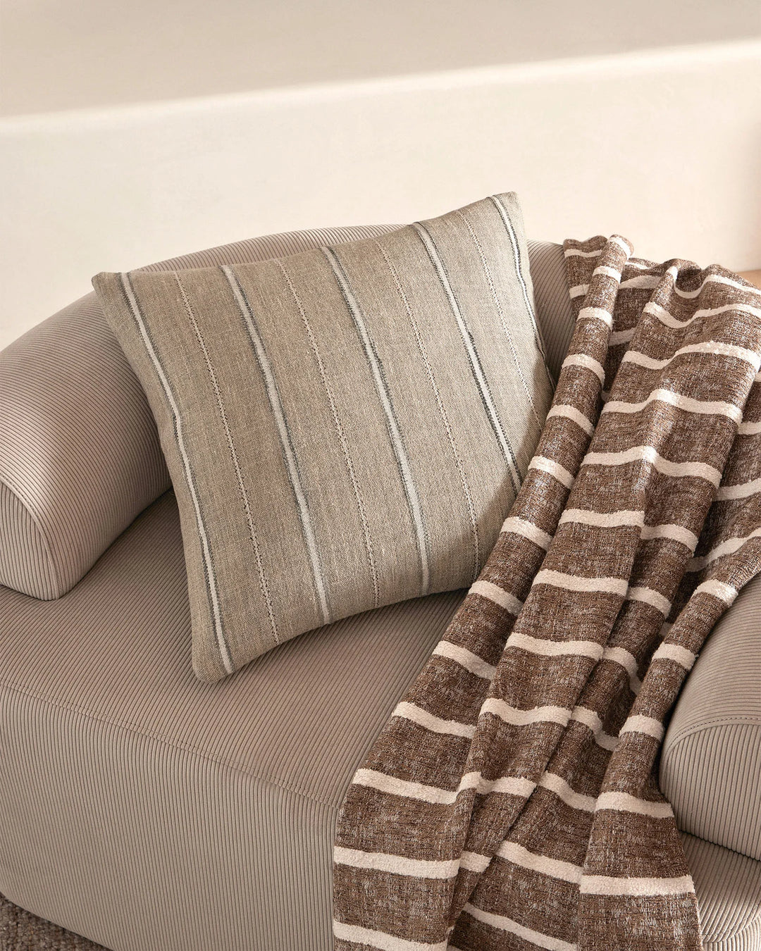 Neutral minimalist seating with striped linen cushion and textured brown-cream striped throw, showcasing soft neutral palette and layered woven textures
