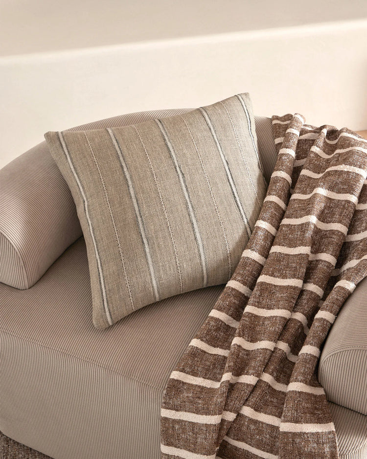 Neutral minimalist seating with striped linen cushion and textured brown-cream striped throw, showcasing soft neutral palette and layered woven textures
