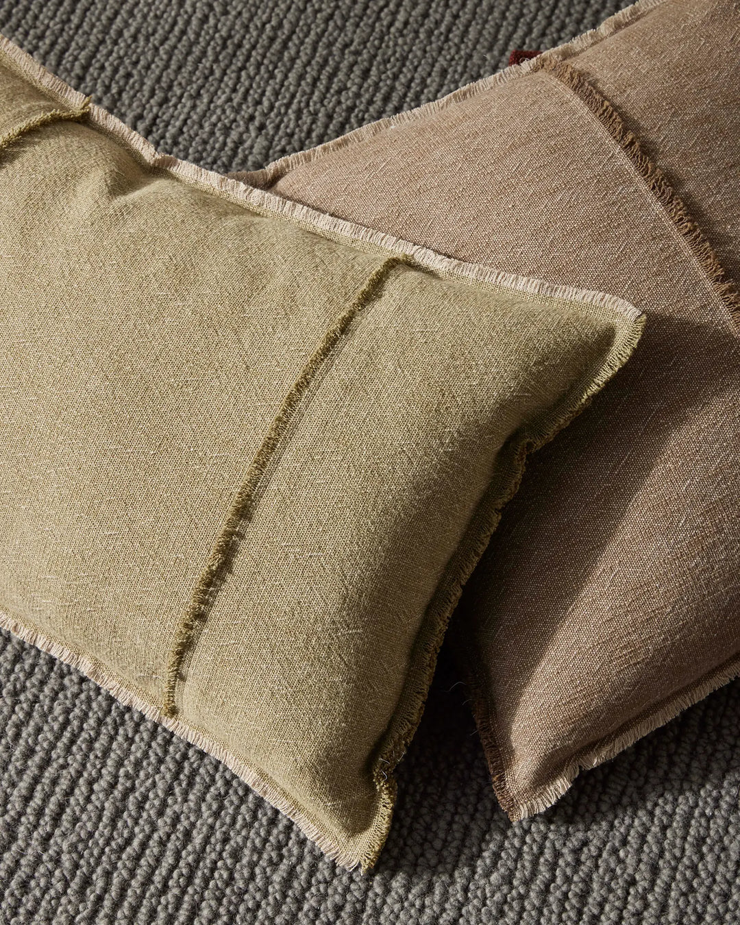 Neutral linen cushions in sage and warm taupe tones layered on textured grey upholstery, showcasing organic weaves and natural fabric textures in earthy, minimalist home styling.