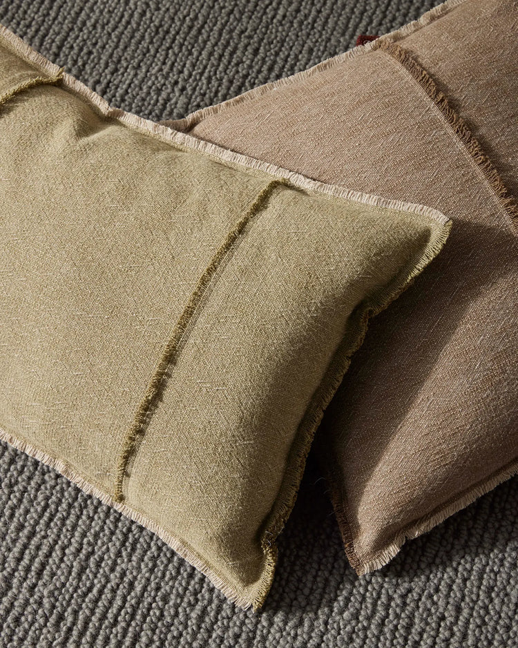 Neutral linen cushions in sage and warm taupe tones layered on textured grey upholstery, showcasing organic weaves and natural fabric textures in earthy, minimalist home styling.
