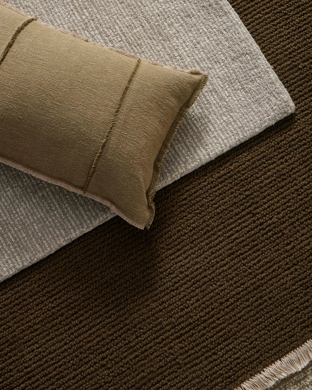 Neutral earth-tone layered lifestyle with Adela Forest cushion on waffle-weave textiles, showcasing warm olive, khaki and soft grey textured fabrics