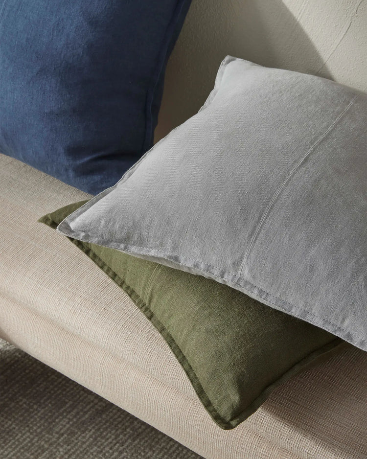 Neutral and sage linen cushions layered on cream upholstered seating, with navy fabric and textured throws creating a relaxed, earthy colour palette