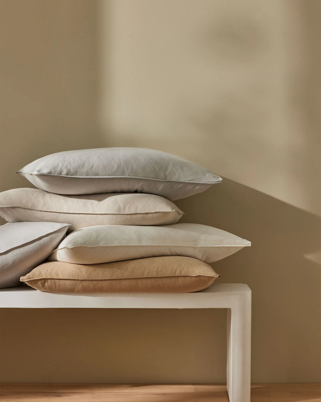 Stacked Ravello Pillowcase Set in neutral linen tones, displaying cream, ivory and warm sand hues against soft taupe wall and wooden floor