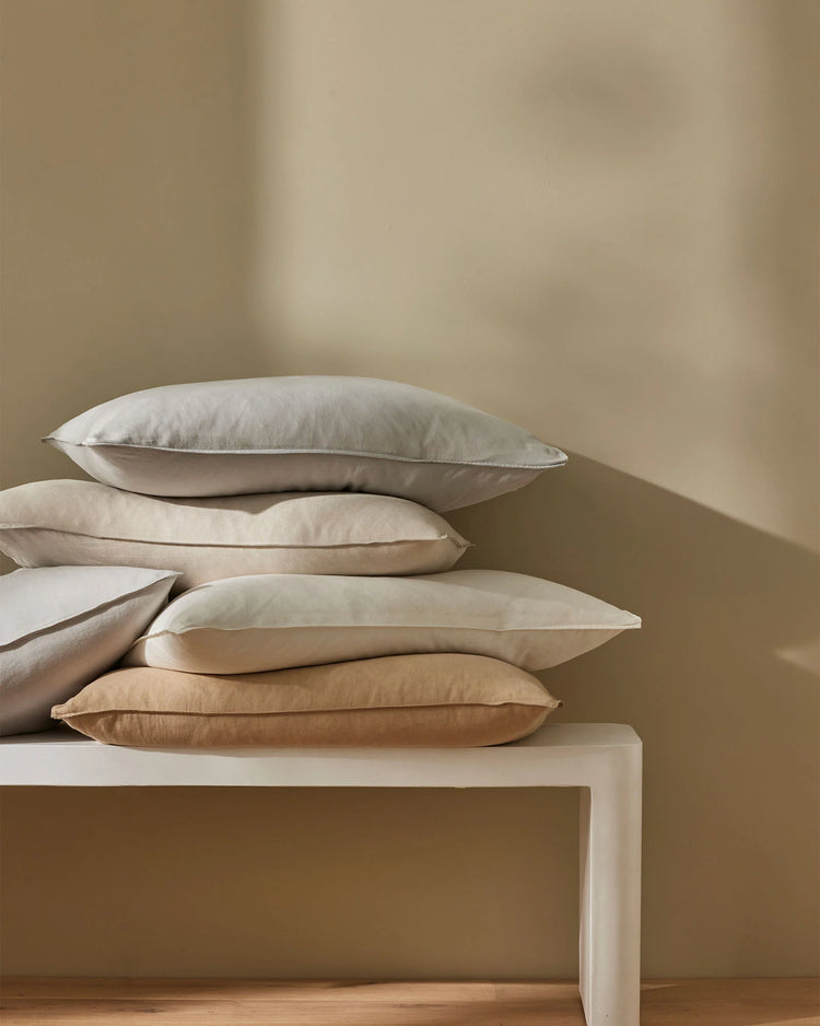 Stacked Ravello Pillowcase Set in neutral linen tones, displaying cream, ivory and warm sand hues against soft taupe wall and wooden floor