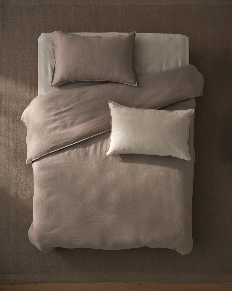 Overhead view of bed styled with neutral linen bedding in warm taupe and cream tones, Ravello Quilt Cover and Fiore cushions creating a serene, minimalist bedroom aesthetic with soft linen textures
