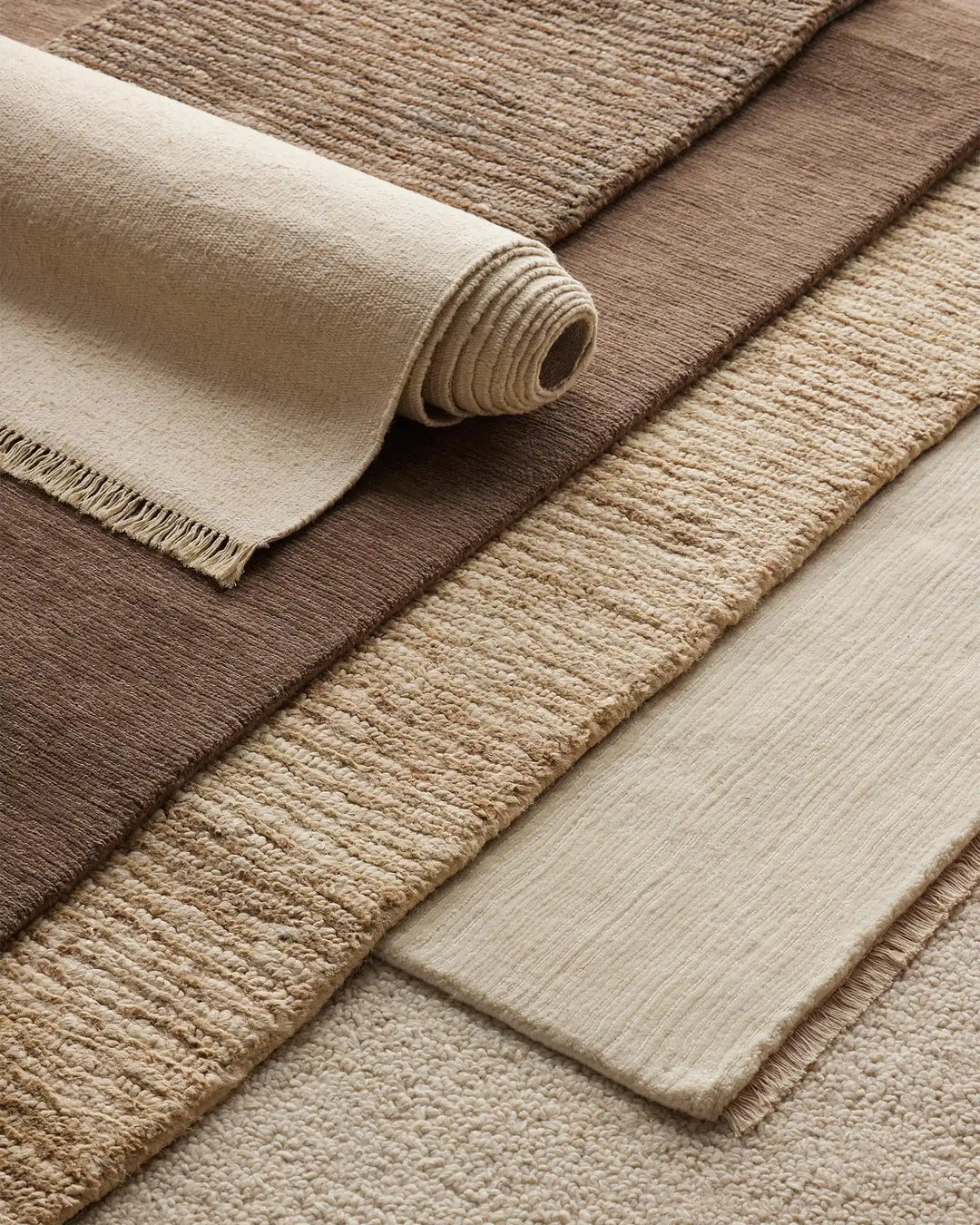 Neutral layered rugs in cream, taupe and warm brown tones showcase textured weaves and natural fibres in an earthy palette, ideal for minimalist interior styling
