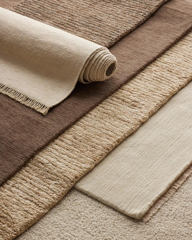 Neutral layered rugs in cream, taupe and warm brown tones showcase textured weaves and natural fibres in an earthy palette, ideal for minimalist interior styling