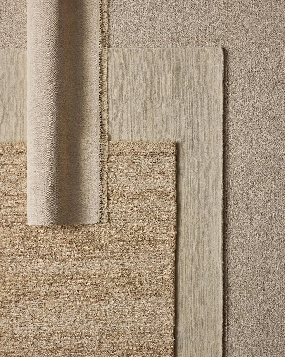 Neutral rug styling with layered textures: woven jute, linen, and wool blends in cream, sand, and taupe tones creating an earthy, minimalist aesthetic