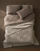 Overhead view of a neutral linen bed with Ravello Coverlet and Pillowcase Set in bone and pebble tones, layered with quilted textures and soft natural light casting shadows on warm taupe walls