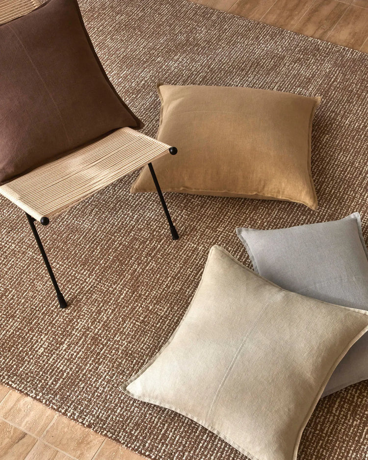 Neutral living room styled with Como linen cushions in sandstone, oatmeal and cocoa tones layered on textured jute rug, beside mid-century chair and wooden flooring
