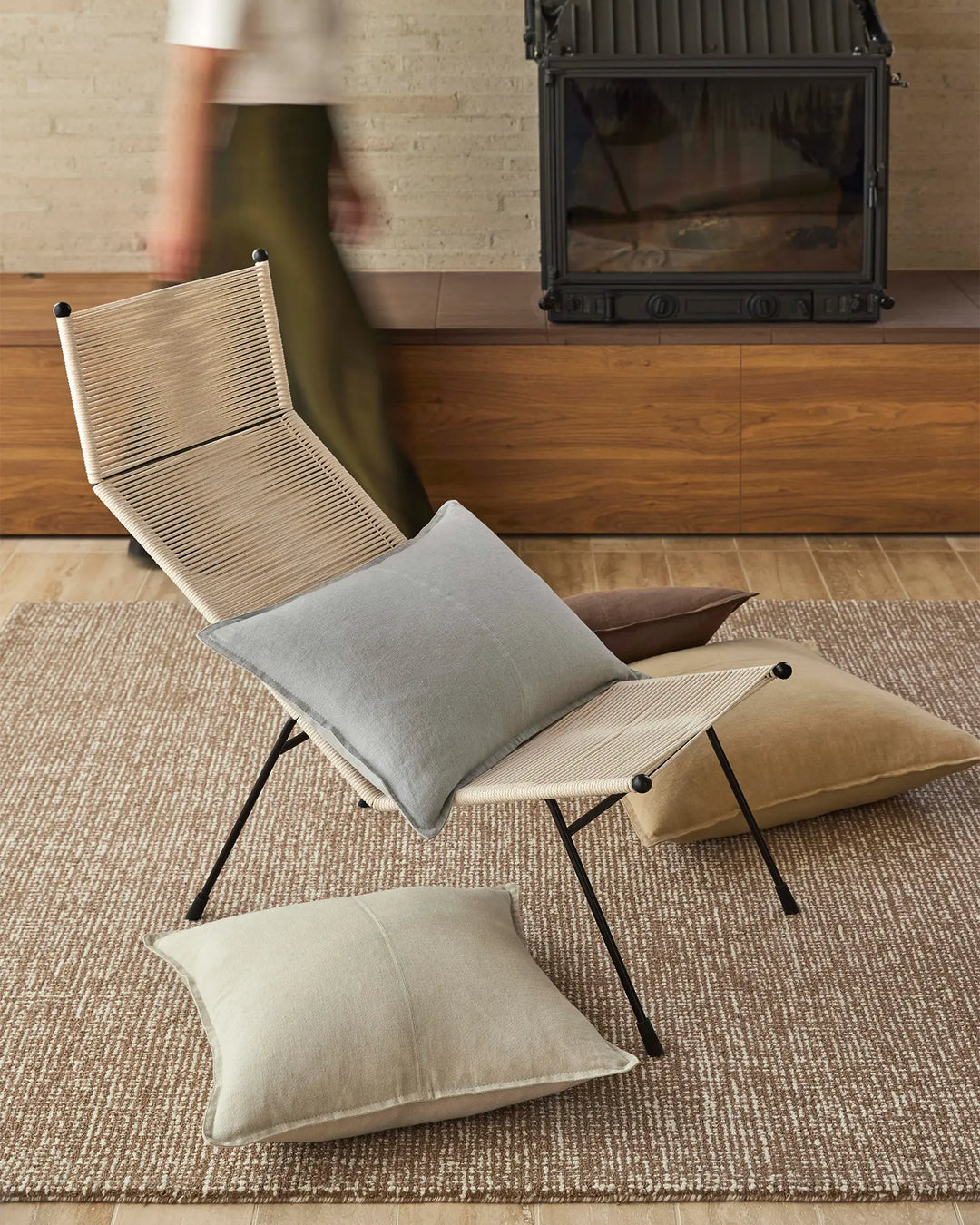 Mid-century lounge setting with natural linen cushions in cream and grey tones layered on wooden chair, neutral textures and warm wood accents