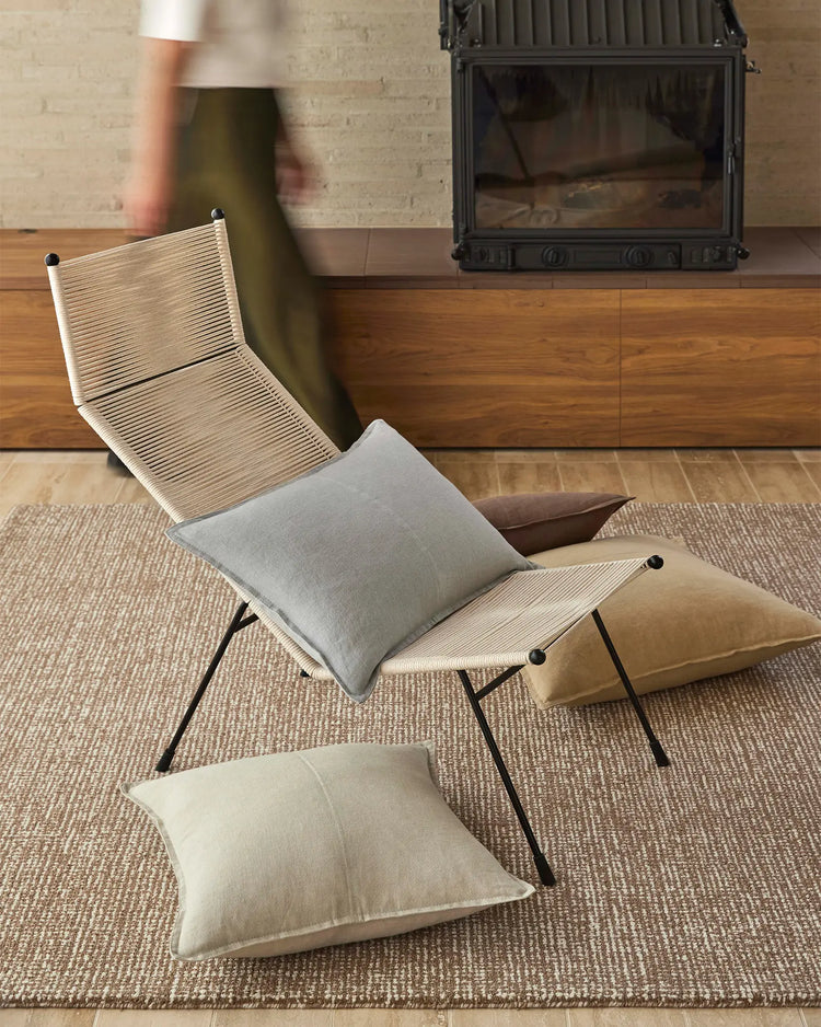 Mid-century lounge setting with natural linen cushions in cream and grey tones layered on wooden chair, neutral textures and warm wood accents