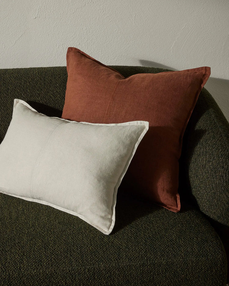 Earthy minimalist styling with oatmeal and terracotta linen cushions layered on a sage green textured sofa against a neutral wall, natural light highlighting linen texture and warm colour palette